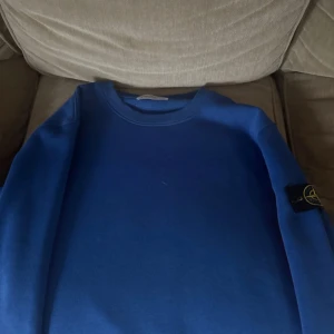 Blå Stone Island sweatshirt - Säljer en blå sweatshirt från Stone Island med klassisk rund hals och den ikoniska loggan på vänster ärm. Tröjan är i mjuk bomull och har en enkel, clean design som passar perfekt till jeans eller joggers. Storlek M, använd fåtal gånger.