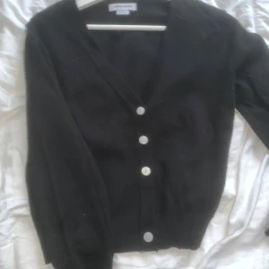 Svart kofta  - Svart kofta från Urban Revivo med v-ringning och knappar framtill. Långärmad och i mjukt stickat material, perfekt för lager på lager. Enkel och stilren design som funkar till allt.