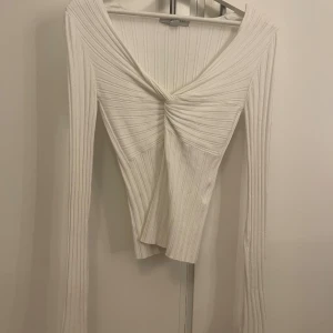 Vit ribbad långärmad topp - Säljer en vit ribbad långärmad topp med snygg twistad detalj framtill och v-ringad hals. Toppen är figurnära och har långa ärmar med stretchigt material som sitter skönt. Perfekt för dig som gillar stilrena och trendiga plagg. Nypris 299❤️