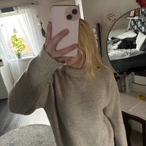 Beige stickad tröja från H&M - Mysig beige stickad tröja från H&M med ribbad struktur och hög krage. Perfekt för kyliga dagar och har långa ärmar som ger en skön och avslappnad vibe. Passar dig som gillar enkel och stilren look.