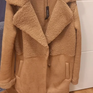 Beige teddyjacka från Boohoo - Säljer en beige teddyjacka från Boohoo med stora kragar och mysigt teddyfoder upptill. Jackan har två fickor framtill och stängs med knappar. Perfekt för dig som gillar oversized och chill stil. Tillverkad i Italien.