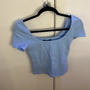 Ljusblå topp från Gina Tricot - Säljer en ljusblå topp från Gina Tricot i storlek XS. Modellen har korta ärmar, bred och djup rundad halsringning samt en croppad passform. Materialet är mjuk bomull som känns skönt mot huden. Perfekt att styla med jeans eller kjol för en fräsch look.