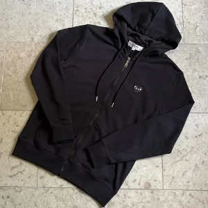 Svart ziphoodie från Cdg Play - Svart ziphoodie från Cdg play i storlek S. Ikoniskt hjärta broderat på bröstet med tryck på ryggen. Nytt och oanvänt skick och fraktas inom 24h✅