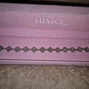 Armband från HIMO - Säljer ett snyggt armband från HIMO Home. Det ena är silverfärgat med glittriga fyrklöverformade länkar, det andra har svarta fyrklöver i rad med silverdetaljer. Perfekta accessoarer för att lyfta din outfit. OBS asken ingår inte