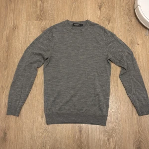 Grå merinoulltröja från Dressmann - Säljer en stilren grå tröja från Dressmann i mjuk merinoull. Tröjan har rund halsringning, lång ärm och en klassisk passform. Perfekt för lager-på-lager och funkar året runt. Enkel och snygg att matcha med det mesta.