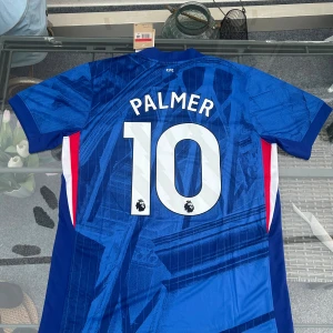 Chelsea FC hemmatröja 25/26 – Palmer #10 (herr L) - Säljer en Chelsea FC hemmatröja säsongen 2025/26, officiell Nike Dri-Fit, med Cole Palmer #10 och Premier League-tryck på ryggen. Tröjan är i herrstorlek L, helt ny med tags kvar och aldrig använd.  Passar både dig som är Chelsea-supporter, samlar på fotbollströjor, eller vill styla en unik streetwear-look med en äkta matchtröja.  ✨ Officiell Nike-produkt ✨ Ny med tags ✨ Palmer #10 – Premier League-print ✨ Storlek L 