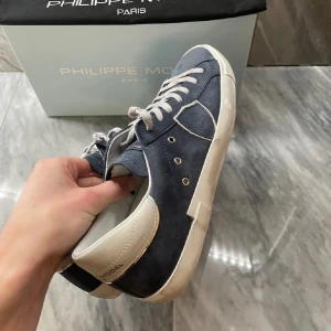 Philippe Model blå sneakers mocka - Snygga sneakers från Philippe Model i marinblå mocka med vita detaljer och snörning. Skorna har en vit platt sula och rund tå, samt en vit hälkappa med logga. Perfekta för dig som gillar stilrena och trendiga sneakers med premiumkänsla. Skicket är 7.5/10. Skriv för fler bilder!