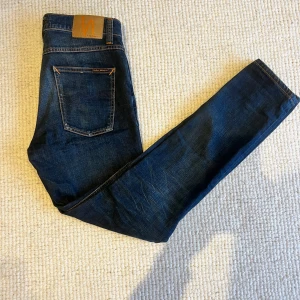 Nudie Jeans blå jeans W29 L30 - Snygga blå jeans från Nudie Jeans med klassisk femficksdesign och orangea sömmar. Modell Lean dean. De är lite små i storleken. 