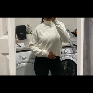 Vit polotröja i stickat material - Säljer en vit polotröja i stickat material med lång ärm och ribbade muddar. Tröjan har en hög krage och en något loose passform, perfekt för kyligare dagar. Enkel och stilren design som är lätt att matcha. Nyskick! 