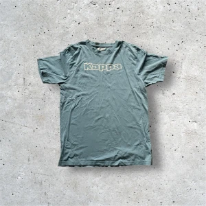 Blå Kappa t-shirt XL - Snygg blå t-shirt från Kappa i storlek XL. Klassisk modell med korta ärmar, rund hals och tryckt Kappa-logga på bröstet. På ena ärmen finns det broderade Kappa-emblemet i vitt. Skön och mjuk bomullskvalitet.