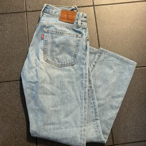 Levi's 501 ljusblå jeans W26 L32 - Klassiska Levi's 501 jeans i ljusblå tvätt med raka ben och normal passform. Jeansen har fem fickor, knappgylf och ikonisk läderpatch bak i midjan. Tillverkade i slitstarkt bomullsjeans, perfekta för en avslappnad och tidlös look. Om