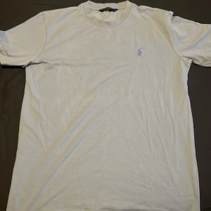 Ljusblå t-shirt från Polo Ralph Lauren - Vit t-shirt från Polo Ralph Lauren med klassisk rund hals och broderad logga på bröstet. Tillverkad i mjuk bomull och har en clean, enkel look som passar perfekt till jeans eller shorts.