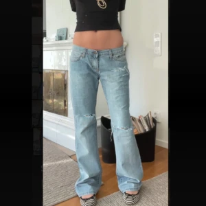 Dallas Jeans ljusblå bootcut jeans med revor - Ljusblå jeans från Dallas Jeans med raka ben och utsvängda där nere. Slitna detaljer vid knäna. Klassisk femficksmodell med normal passform och låg midja. Jeansen har en snygg vintagekänsla och är tillverkade i bomull. Perfekta för dig som gillar en avslappnad och trendig look.