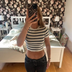 Randig croppad topp från Zara - Säljer en fräsch croppad topp från Zara i storlek S. Toppen är vit med mörkblå horisontella ränder, har rund hals och korta ärmar. Materialet är mjukt och ribbat, vilket gör den både bekväm och snygg. Perfekt för dig som gillar en clean och trendig look.