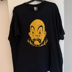 Svart t-shirt Joker Brand XXL och keps  - Svart t-shirt från Joker Brand i storlek XXL med stor guld clown-tryck på bröstet. Klassisk rund hals och korta ärmar. T-shirten har en loose passform och är tillverkad i mjuk bomull. Perfekt för dig som gillar streetwear och unika prints. Och keps med guld 
