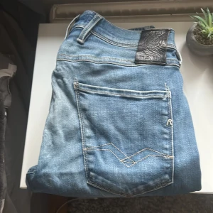 Blå Replay Anbass Hyperflex jeans - Säljer ett par blå Replay Anbass Hyperflex jeans i klassisk tvätt. Jeansen har fem fickor, snygga kontrastsömmar och Replay-logga på fickan. Modellen är slim och stretchig för extra komfort. Perfekta för dig som gillar en modern och stilren look.