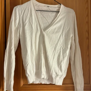 Vit kofta med knappar  - En stilren vit kofta med v-ringning och knäppning framtill. Långärmad modell i mjuk bomull, perfekt att slänga över en t-shirt eller linne. Enkel och clean look som passar till det mesta.