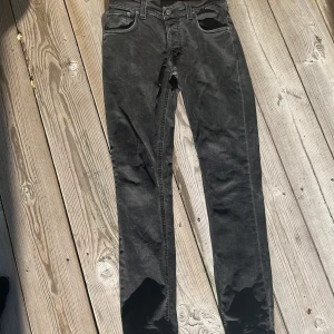 Svarta jeans från Nudie Jeans, 28/30 - Svarta jeans från Nudie Jeans i modellen GRIM TIM. Jeansen har en rak passform med normal midja och är tillverkade i mjukt denimtyg. Snygga detaljer med Nudie-logga på bakfickan och diskreta sömmar. Perfekta för en stilren och avslappnad look. Skriv om fler bilder behövs!