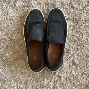 Svarta loafers från Pace - Svarta loafers från Pace med vit sula och ovandel i mocka. Skorna har en klassisk, stilren design med rund tå och platt sula. Perfekta att slänga på sig till jeans eller chinos för en avslappnad look.