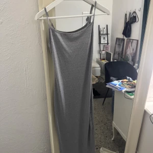 Grå ribbad långklänning med smala axelband - Säljer en stilren grå långklänning med smala axelband och ribbad struktur. Klänningen har en tight passform och är perfekt för dig som gillar clean stil. Materialet är mjukt och stretchigt, vilket gör den superbekväm att bära. Passar upp till M skulle jag säga.