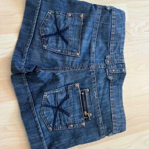 Mörkblå jeansshorts från TRF Denim - Säljer ett par mörkblå jeansshorts från TRF Denim med snygga detaljer som kontrastsömmar, dekorativa nitar och en cool dragkedja på bakfickan. Shortsen har normal till låg passform, klassiska fickor och bälteshällor. Perfekta för en chill sommarstil! Bara skriv om ni har några frågor eller vill ha mått!💕