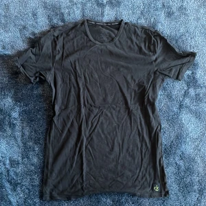 Svart t-shirt från Calvin Klein - Svart t-shirt från Calvin Klein med rund hals och diskret CK-logga nere vid fållen. Klassisk passform och tillverkad i mjuk bomull som känns skön mot huden. Perfekt för dig som gillar stilrena och enkla plagg med en touch av designer.