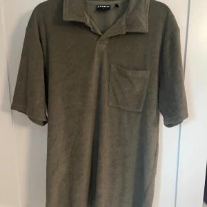 Olivgrön frotté t-shirt från Firefly - Olivgrön t-shirt från Firefly i mjuk frotté med klassisk krage och bröstficka. Modellen är kortärmad och har en relaxed vibe, perfekt för chill dagar. Enkel och stilren utan mönster, passar dig som gillar basic men ändå vill sticka ut lite.