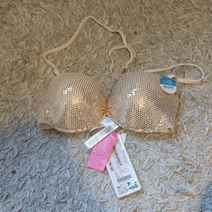 Glittrig bikiniöverdel - Supersnygg bikiniöverdel i beige med glittriga paljetter över hela ytan. Balkongmodell med vadderade kupor och justerbara axelband. Perfekt för att sticka ut på stranden eller vid poolen. Säljs med originaltaggar kvar. (179 kr från början)