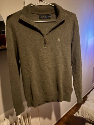 Grå Grön half zip tröja från Polo Ralph Lauren - Snygg grå/grön långärmad tröja från Polo Ralph Lauren med half zip och klassisk krage. Tröjan har en broderad logga på bröstet och är tillverkad i mjukt stickat material som passar perfekt för kyliga dagar. Enkel och stilren design som funkar till många outfits. Väldigt fint skick, sitter rätt storleksmässigt och om du är ca 175cm kommer den sitta bra. Ge prisförslag!
