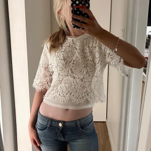 Vit spetsblus från Amisu XS - Säljer en vit blus från Amisu i storlek XS. Blusen är croppad med korta ärmar och har ett detaljerat blommigt spetsmönster. Perfekt för dig som gillar romantisk och feminin stil. Superfin att matcha med jeans eller kjol!