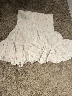  Lager 157 kjol - Supersöt vit kortkjol från 157 i storlek XS med små blommor i rosa och blått. Kjolen har bred smock upptill och flera volanger som ger en flowy känsla. Perfekt för dig som gillar romantisk och feminin stil. 