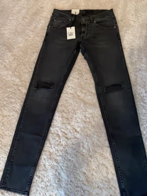 Svarta jeans Tiger of Sweden - Svarta jeans från Tiger of Sweden med slitna detaljer vid knäna. Klassisk femficksmodell med dragkedja och knapp i midjan. Jeansen har en mörk tvätt och är tillverkade i stretchigt bomullsmaterial för extra komfort. Nypris: 1600kr