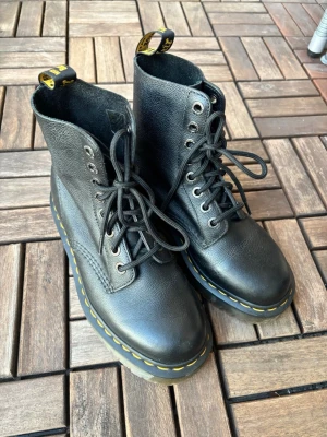 Svarta Dr. Martens boots i skinn - Säljer ett par klassiska svarta Dr. Martens boots med snörning och rund tå i storlek 38. Dessa är varianten i mjukt läder samt med en liten platform. Har använts ett fåtal gånger och är som nya. Lite dammiga men det löser jag! 🫡 (Kan skickas med PostNords spårbara frakt). 