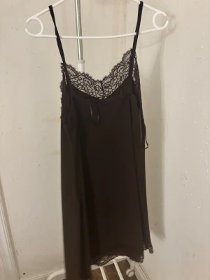 Brun linnetopp med spetsdetaljer - Säljer en brun linnetopp med tunna axelband och vacker spets längs halsringningen och nederkanten. Toppen har en slät, mjuk yta och är ärmlös med en feminin och stilren look. Perfekt för dig som gillar enkla men snygga detaljer.