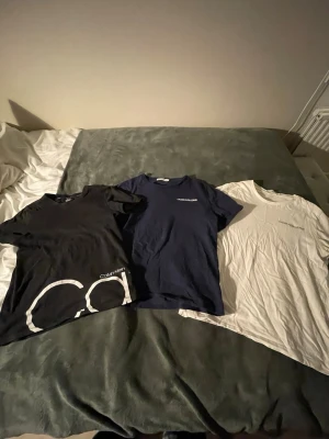 3-pack Calvin Klein t-shirts - Säljer tre snygga t-shirts från Calvin Klein i olika färger: svart med stor logga st 10-12, marinblå med diskret tryck st 12 och vit med liten logga st 14. Alla har rund hals och korta ärmar, tillverkade i mjuk bomull. Perfekt för dig som gillar stilrena och klassiska plagg.