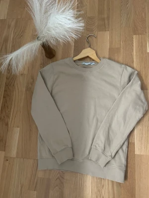 Beige sweatshirt från Lager 157 - Säljer en beige sweatshirt från Lager 157 i storlek 160. Tröjan har rund hals, ribbade muddar vid ärmslut och nederkant samt ett diskret X-detalj vid halsen. Mjuk insida i bomullsmix, perfekt för chill dagar.
