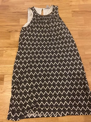 Svartvit mönstrad klänning H&M XS - Svartvit klänning från H&M i storlek XS med rutigt mönster och ärmlös. Rund halsringning med guldfärgad metall-detalj framtill och öppning bak vid nacken. Perfekt nu till nyår!! Ny med prislapp
