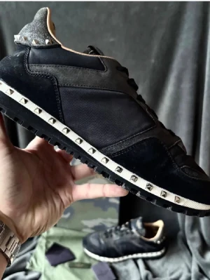 Valentino Garavani Rockrunner sneakers - Säljer ett par svarta Valentino Garavani Rockrunner sneakers med coola nitar längs sulan. Skorna har en mix av mocka och textil, snörning och en chunky gummisula. Märkeslogga på plösen och snygga detaljer som ger en lyxig vibe.