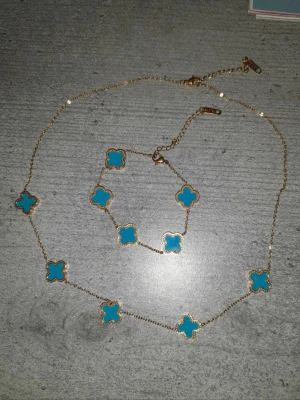 blått halsband och armband - Säljer ett matchande set med halsband och armband i guldton med blå fyrklöverformade hängen. Det är rostfritt. Kedjan är tunn och smyckena har en elegant, ungdomlig vibe