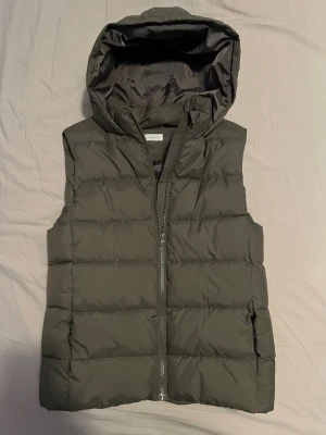 Väst med luva - Snygg mörkgrå dunväst från MNG med stor vadderad huva och dragkedja framtill. Västen har quiltad design och är perfekt för lager-på-lager under kyliga dagar. Enkel och stilren look som passar till det mesta.