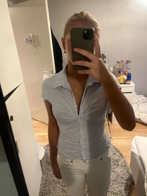 Ljusblå och vit randig skjorta - Snygg kortärmad skjorta med ljusblå och vita ränder. Skjortan har klassisk krage, knappar framtill och figurnära passform. Perfekt till jeans eller kjol för en fräsch look. Materialet känns lätt och skönt mot huden.
