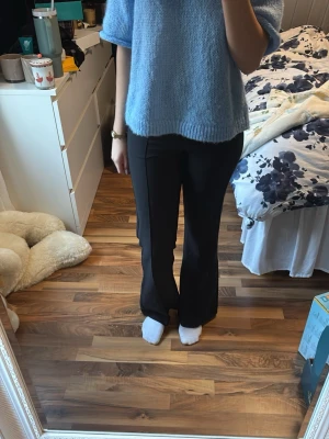 Svarta bootcut kostymbyxor - Säljer ett par svarta kostymbyxor med bootcut-snitt och låg midja. Byxorna har en klassisk rak passform med lätt utsvängda ben och är gjorda i ett slätt material som ger en clean look. Perfekta om du gillar stilrena och tidlösa vibes.