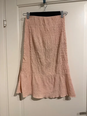 Ljusrosa midikjol från Gina Tricot - Säljer en ljusrosa långkjol från Gina Tricot i storlek XS. Kjolen har en skrynklig, texturerad yta och är lätt utsvängd nedtill. 