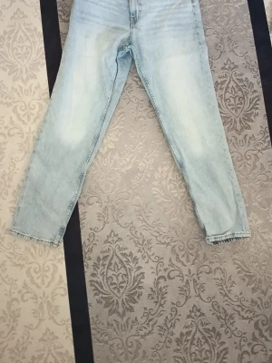 Ljusblå tapered jeans från H&M - Säljer ett par ljusblå jeans från H&M med relaxed fit och tapered ben. Jeansen har justerbar midja och klassisk femficksdesign. Perfekta för dig som gillar en avslappnad men ändå snygg stil. Materialet är klassisk denim i bomull.