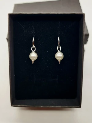Silvriga örhängen med pärlor och spikes - Coola örhängen i silverfärg med rund pärla och liten spetsig detalj under. Perfekt för dig som gillar att mixa klassiskt med edgy stil. Hängande modell som ger en snygg touch till din look.