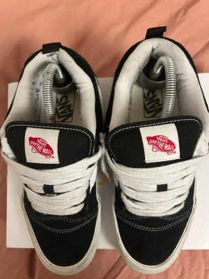 Svarta Vans Old Skool sneakers - Svarta Vans Old Skool sneakers med vit sula och vit sidostripes. Klassisk modell med tjocka vita snören och tydlig Vans Off The Wall-logga på plösen. Skorna har rund tå och är tillverkade i mocka och canvas med kontrasterande vita sömmar. ( Ingen Box)