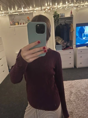  kabelstickad tröja - Säljer en vinröd kabelstickad tröja med rund hals och lång ärm. Tröjan har ett snyggt flätmönster över hela och sitter normalt på kroppen. Perfekt för alla årstider🫰