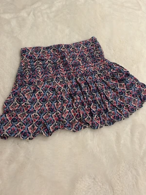 Blommig kortkjol från Zara - Supersöt kortkjol från Zara med blommigt mönster i blått, rosa och vitt. Kjolen har en smockad midja och volangig nederkant som ger en flowy känsla. Perfekt för dig som gillar färg och mönster! Storlek 140 men passar definitivt upp mot 155 (eller mer).🫰🏼🥰