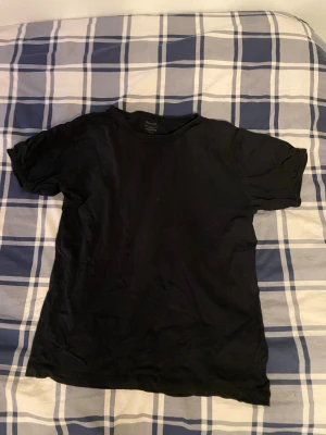 Svart basic t-shirt från Uniqlo - En svart, klassisk t-shirt från Uniqlo i mjuk bomull. Modellen är kortärmad med rund hals och har en clean, enkel look som funkar till allt. Perfekt för dig som gillar minimalistisk stil och vill ha en skön t-shirt i garderoben.