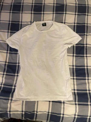 Vit basic t-shirt från 1st Premium - En klassisk vit t-shirt från 1st Premium Basic i storlek small. T-shirten har rund hals och korta ärmar, perfekt för en clean och enkel stil. Tillverkad i mjuk bomull som känns skön mot huden. Passar dig som gillar minimalistiska plagg och vill ha en enkel look.